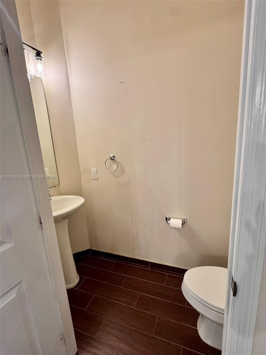 Pedestal sink with chrome faucet, wood-finish tile flooring, wall-mounted light fixture, and polished chrome hardware