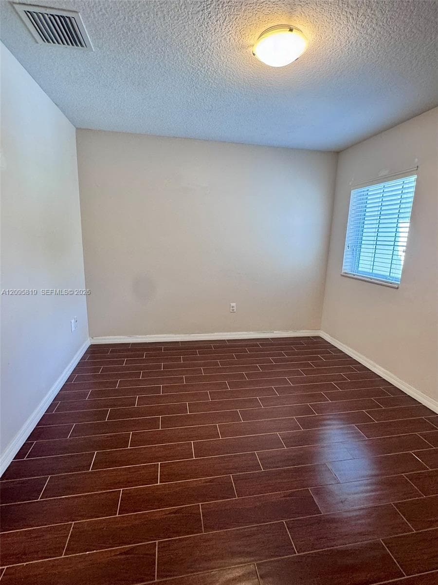 Interior room featuring wood-finish tile flooring, neutral wall paint, and a window with horizontal blinds