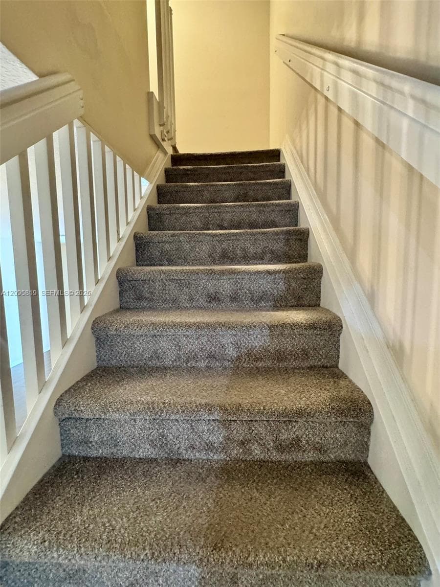 Staircase featuring wall-to-wall carpeting, white painted wooden balusters, and a matching handrail