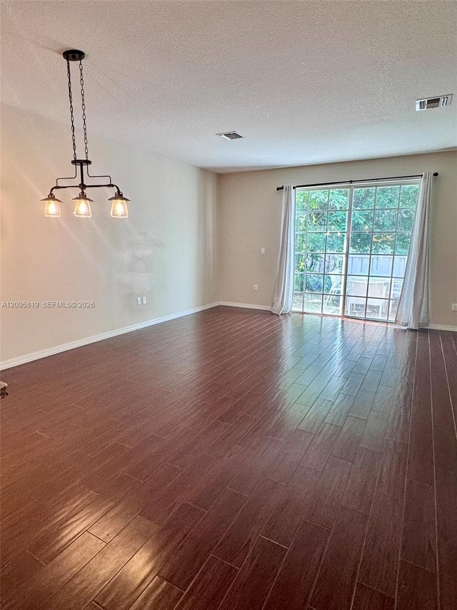 Wood-finish flooring, industrial-style three-light pendant fixture, and sliding glass door with external patio access