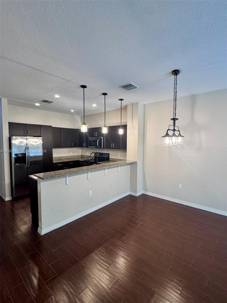 Kitchen featuring dark cabinetry, stone-surface countertops, wood-finish flooring, and multi-light hanging pendant fixtures