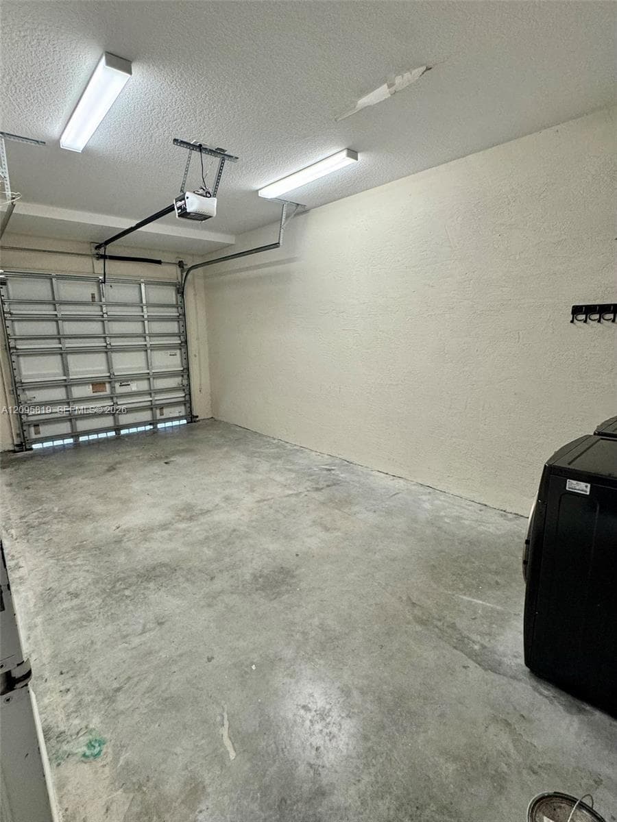 Garage space featuring textured walls, concrete flooring, linear fluorescent lighting, and an overhead garage door opener