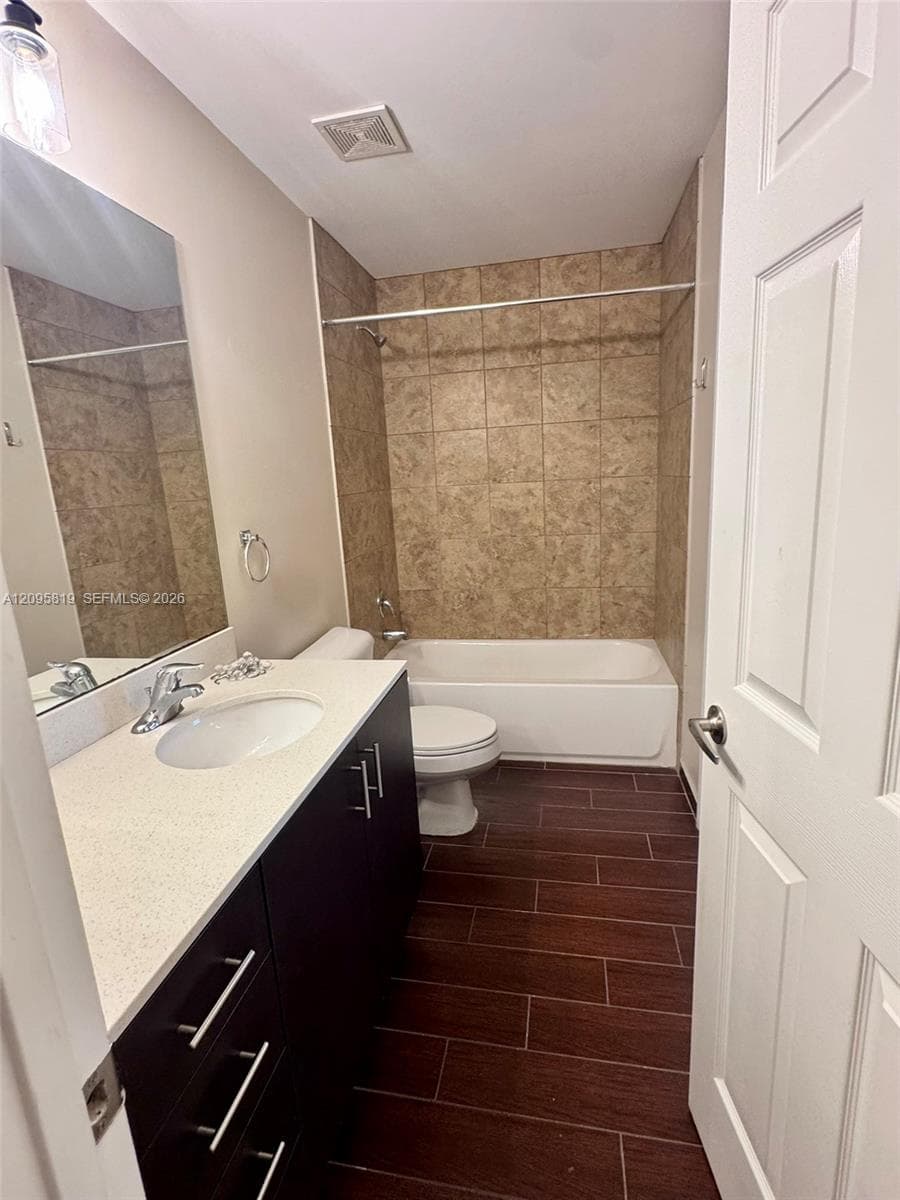 Modern vanity with an integrated sink and light-colored countertop, dark wood-finish cabinetry, floor-to-ceiling tile surround in the tub enclosure, and wood-finish flooring