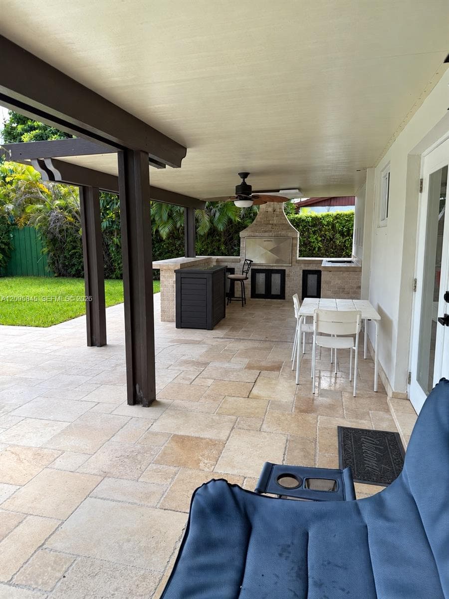 Covered patio featuring stone-tiled flooring, a built-in outdoor kitchen with a stone-finish grill surround, and a ceiling-mounted fan