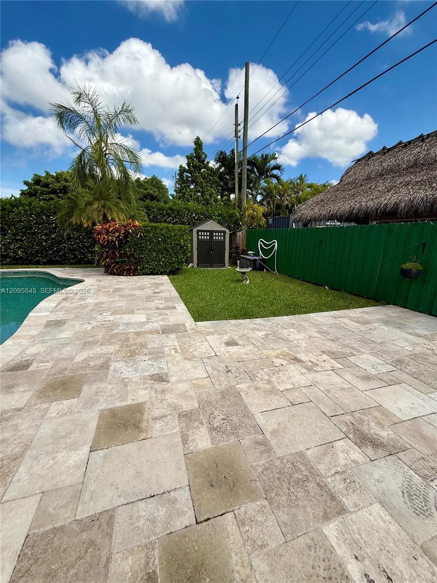Outdoor area featuring a swimming pool, natural stone paver decking, manicured lawn, and perimeter privacy fencing