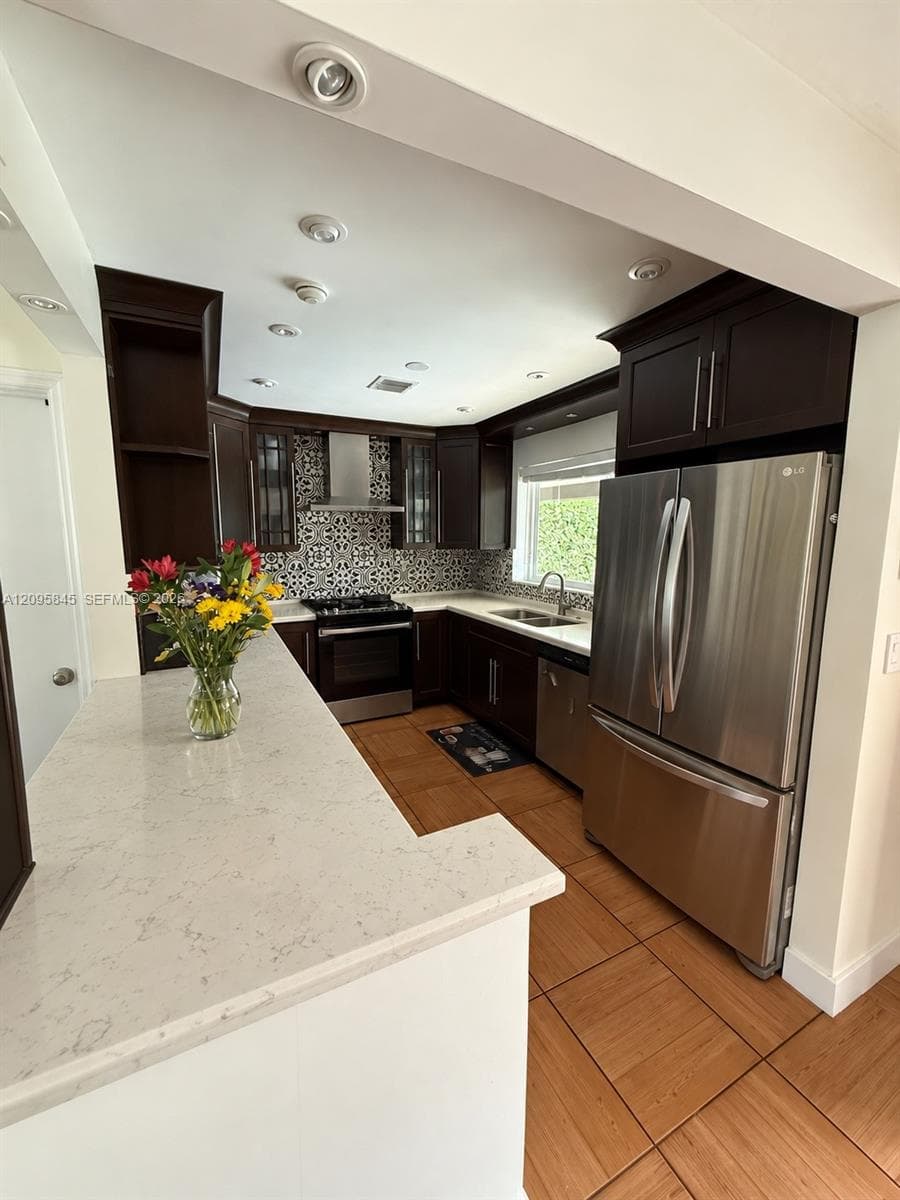 Kitchen featuring dark wood cabinetry, quartz countertops, patterned tile backsplash, stainless steel appliances, and recessed lighting