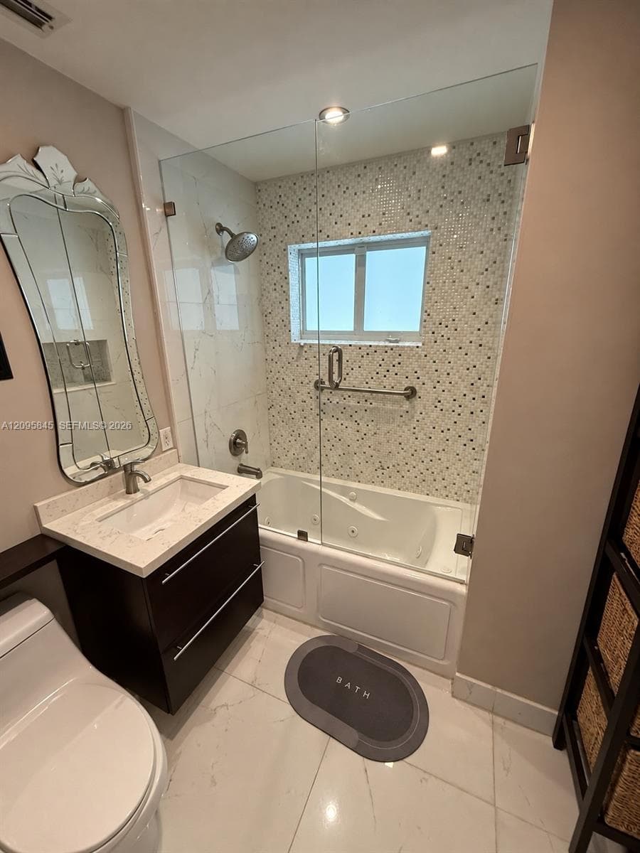 Bathroom featuring a floating vanity with a stone countertop, an integrated jetted soaking tub with a frameless glass enclosure, a mosaic tile tub surround, and porcelain tile flooring