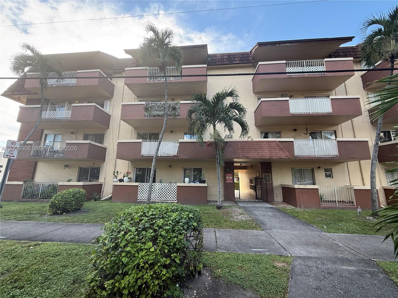 Multi-story residential building featuring private balconies with decorative railings, concrete walkways, and mature landscaping