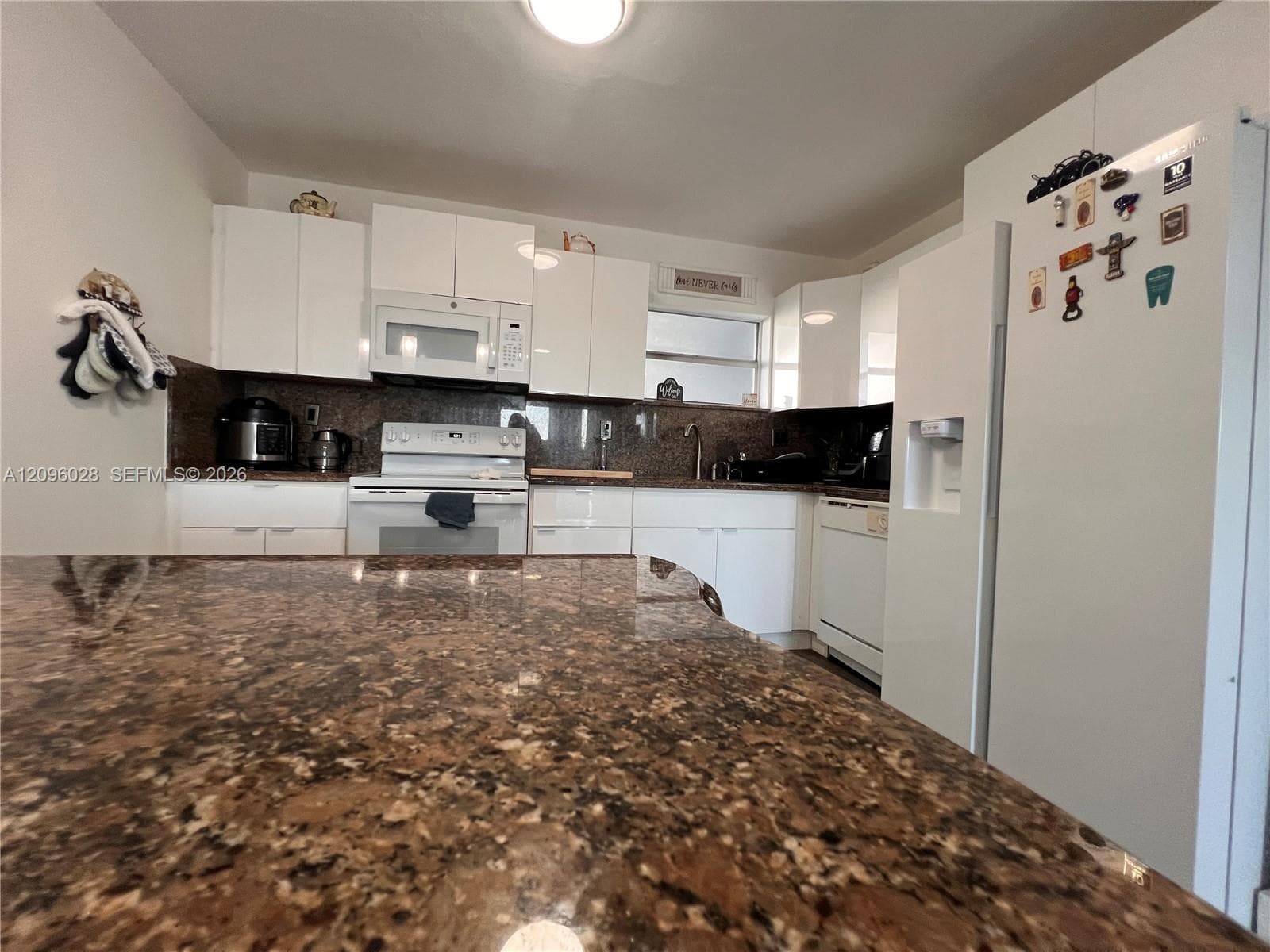 Kitchen featuring white cabinetry, stone-finish countertops, an island, and integrated white appliances