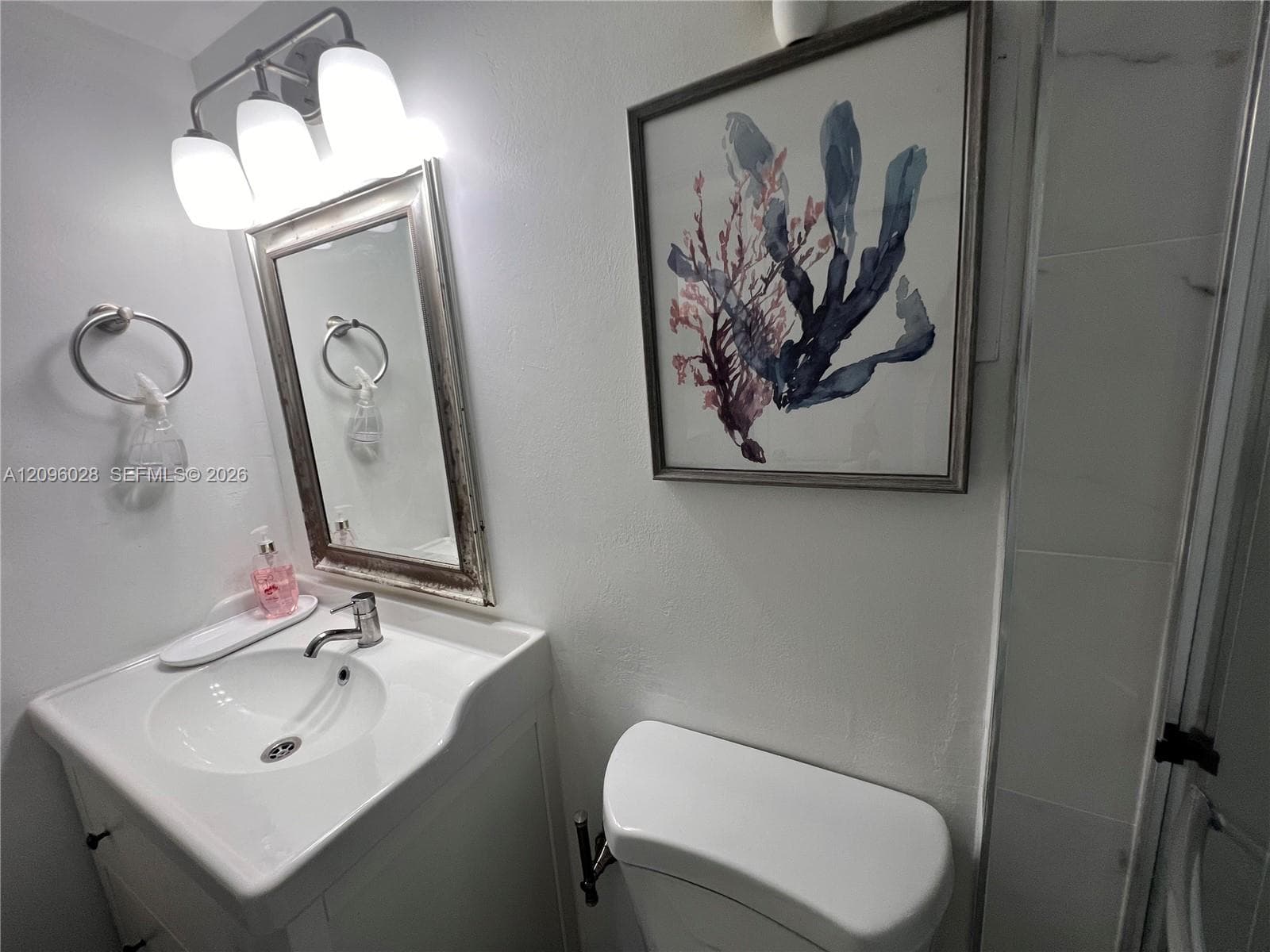 Vanity featuring a white integrated sink, polished metal faucet, three-light overhead fixture, and rectangular mirror