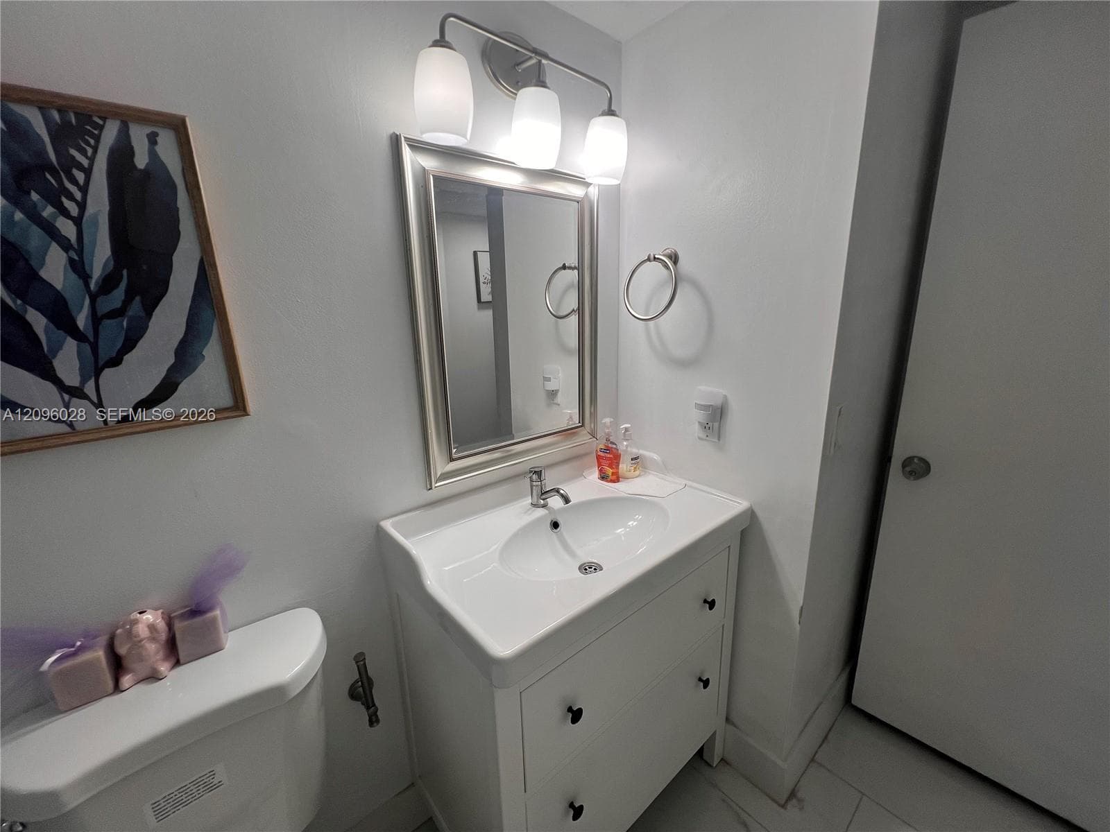 Vanity with integrated porcelain sink, three-light polished chrome fixture, framed wall mirror, and ring towel holder