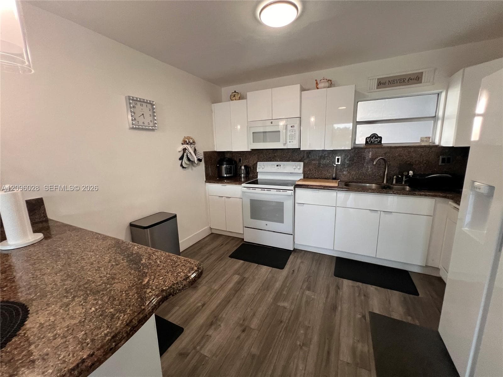 Kitchen featuring high-gloss white cabinetry, stone-finish countertops, wood-finish flooring, and a stainless steel sink with an integrated faucet