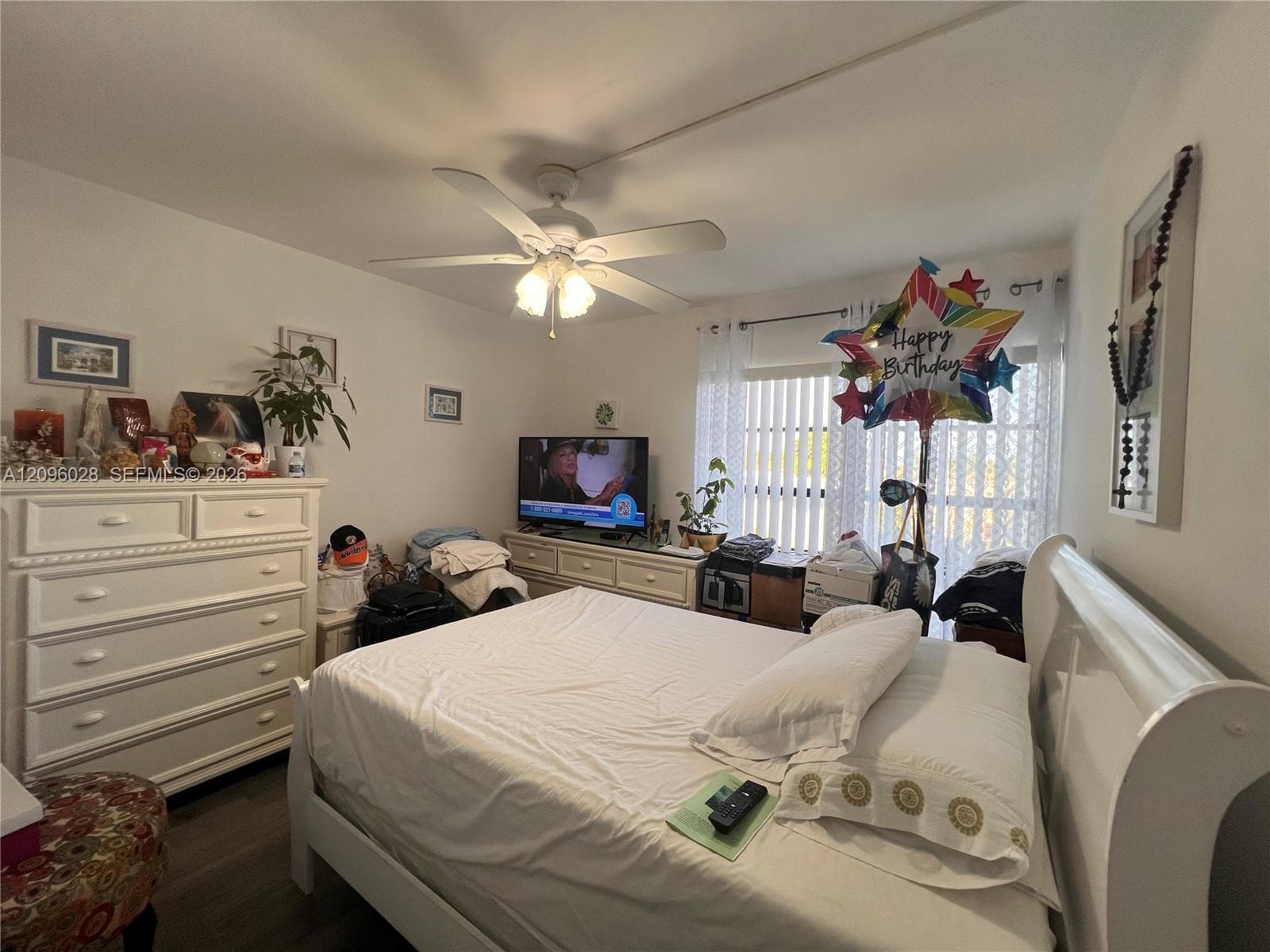 Room featuring wood-finish flooring, a white ceiling fan with integrated lighting, and vertical window blinds
