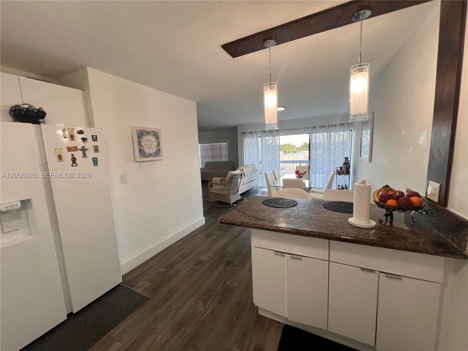 Kitchen featuring a breakfast bar with stone-finish countertop, white cabinetry, wood-finish flooring, and dual hanging pendant lights