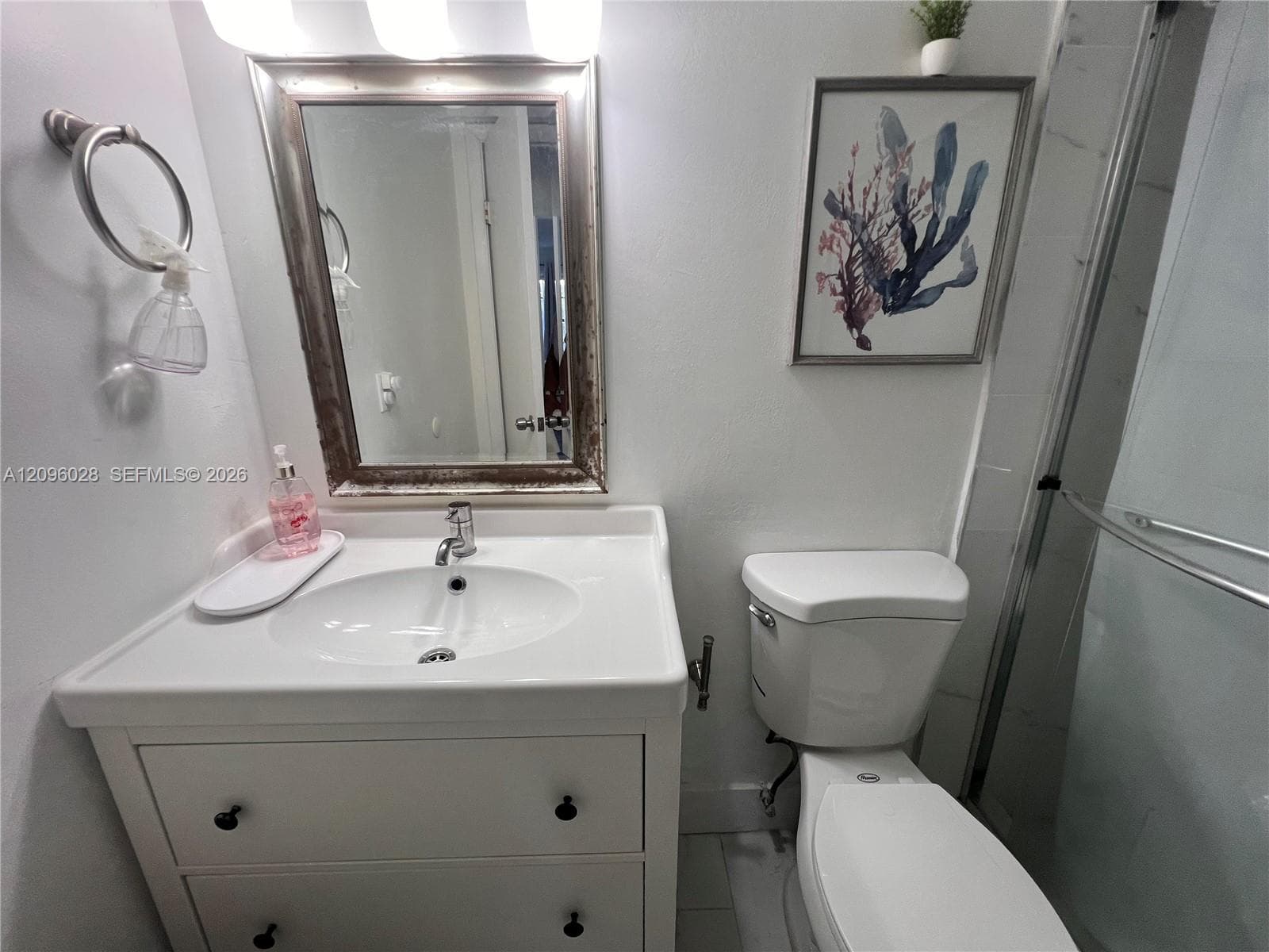 White vanity with an integrated basin, brushed metal hardware, wall-mounted mirror, overhead light fixture, and walk-in shower with sliding glass doors
