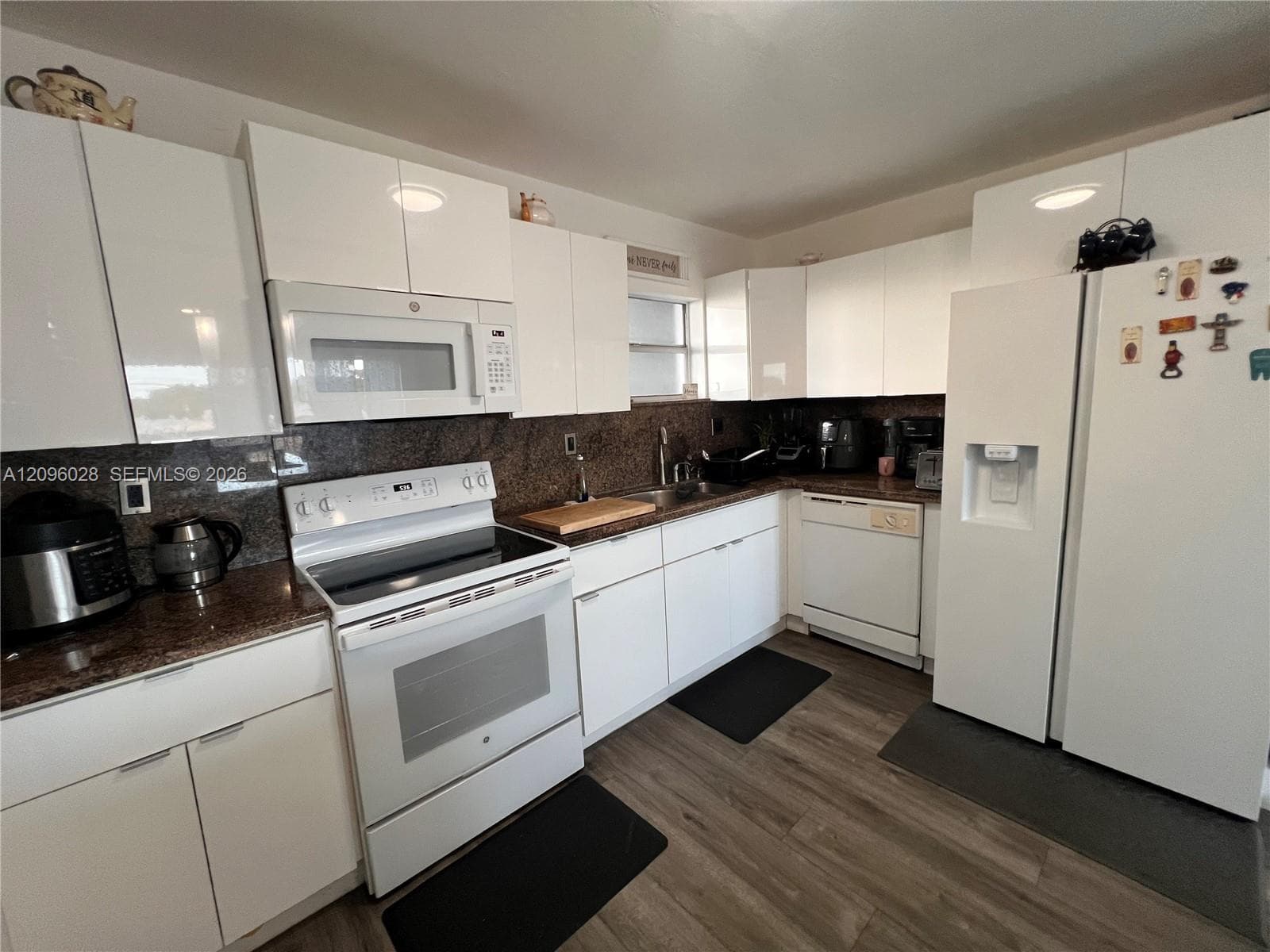 Kitchen featuring high-gloss white cabinetry, stone countertops, wood-finish flooring, and white appliances