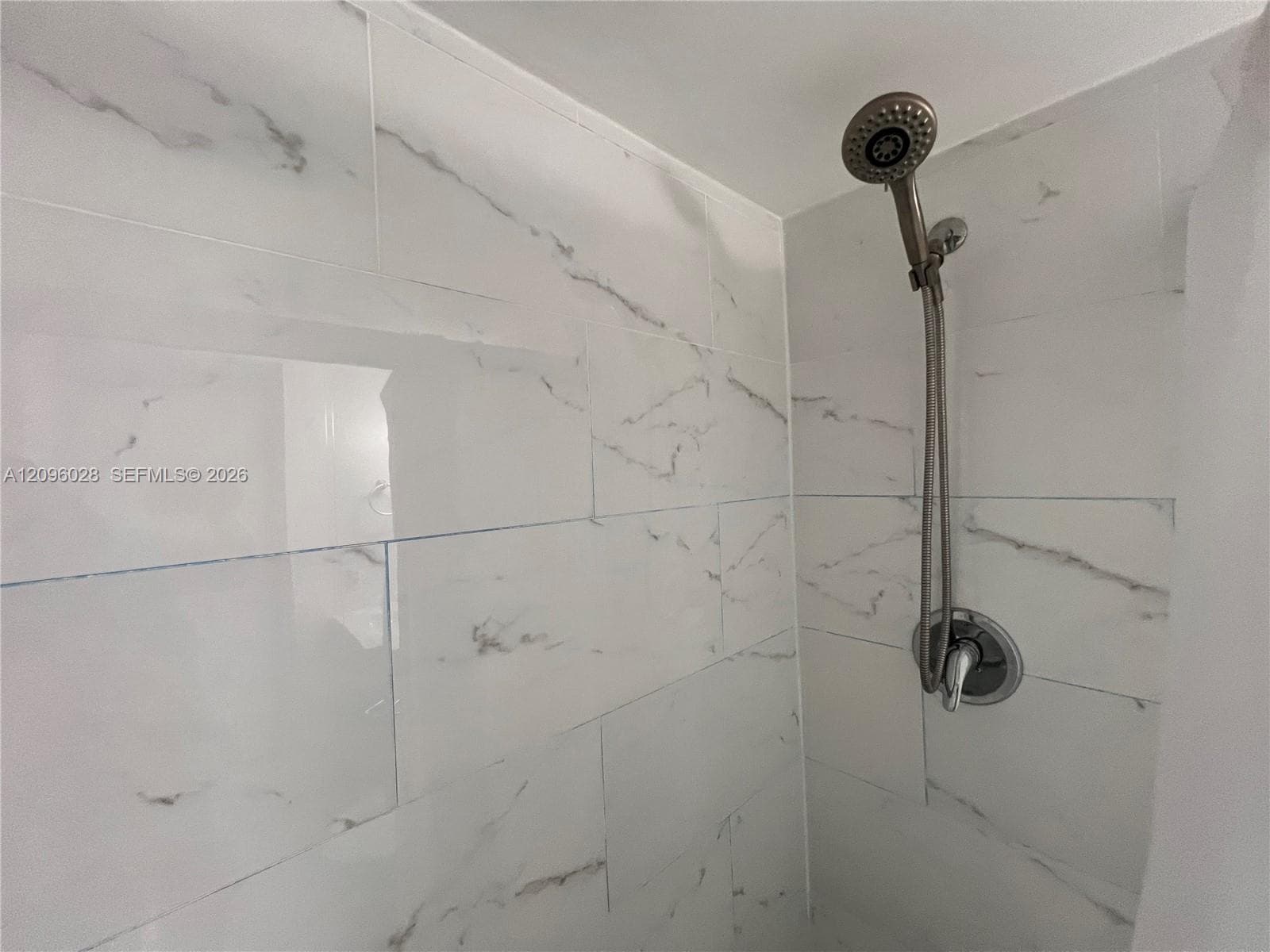 Shower enclosure featuring large-format veined tile surround, adjustable handheld shower head, and single-handle mixing valve