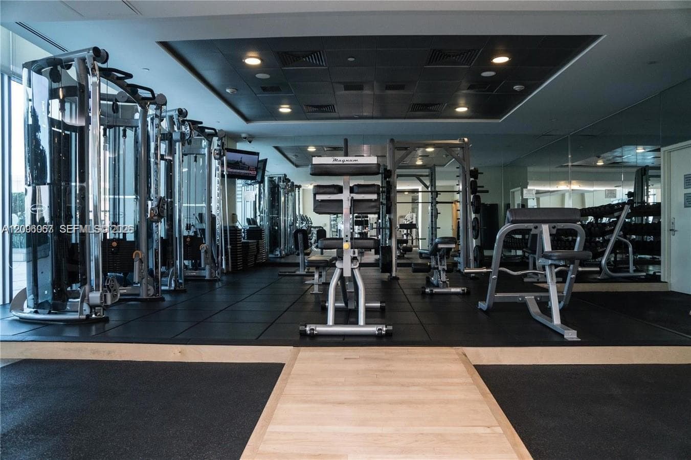 Fitness center with extensive equipment, rubber flooring, mirrored walls, and recessed lighting