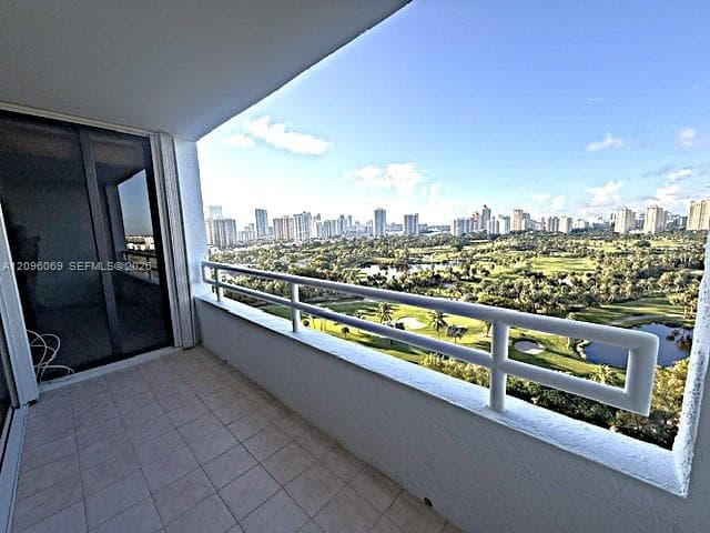 Private balcony featuring a tiled floor and a horizontal metal railing, overlooking a golf course and skyline