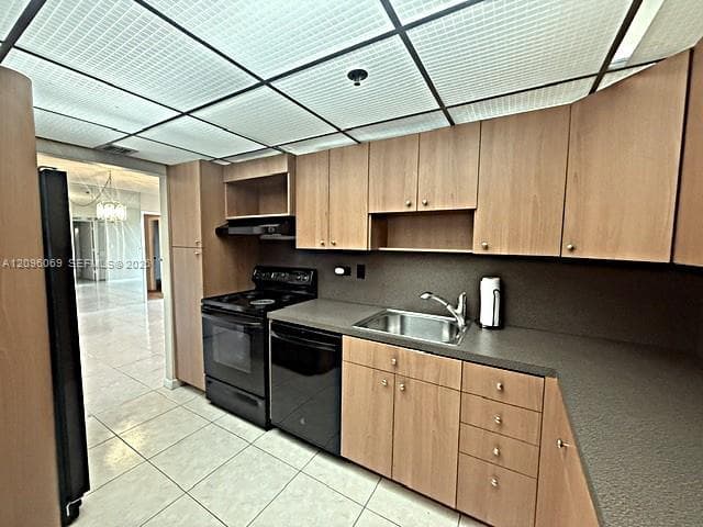Kitchen featuring light wood-finish cabinetry, solid-surface countertops, integrated stainless steel sink with a swivel faucet, and full-size black appliances including an oven range and dishwasher