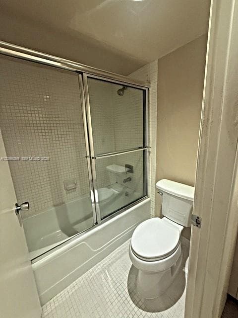 Bathroom featuring a shower-tub combination with a glass sliding enclosure, white mosaic wall tile, and a standard-height toilet