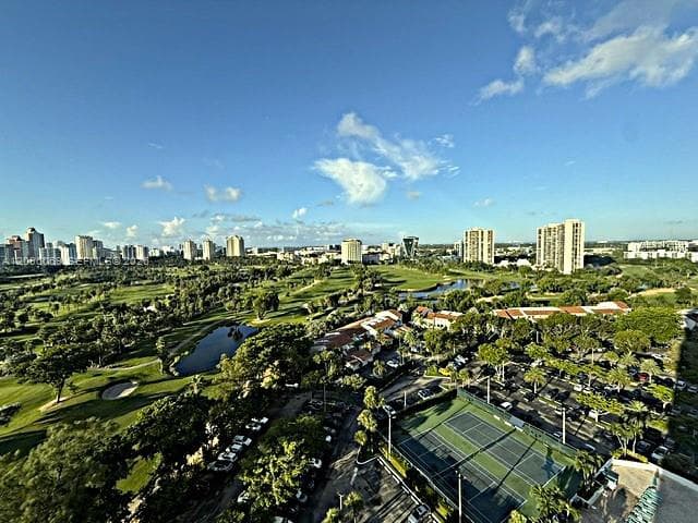 Elevated perspective featuring expansive golf course fairways, water hazards, mature trees, and an on-site tennis court