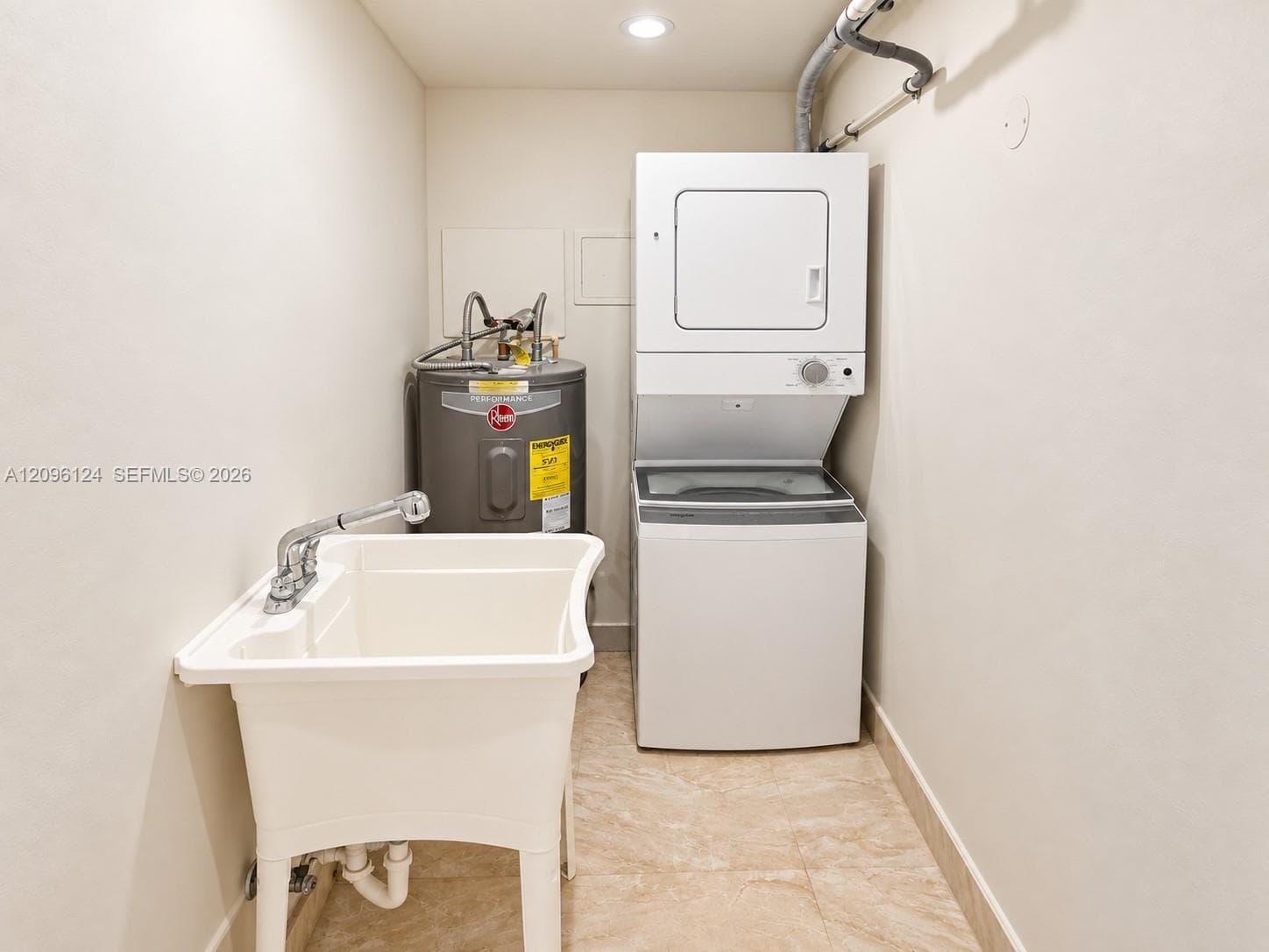 Utility area featuring a stacked laundry unit, a deep basin utility sink with a chrome faucet, and a tank-style water heater, set against stone-finish tile flooring