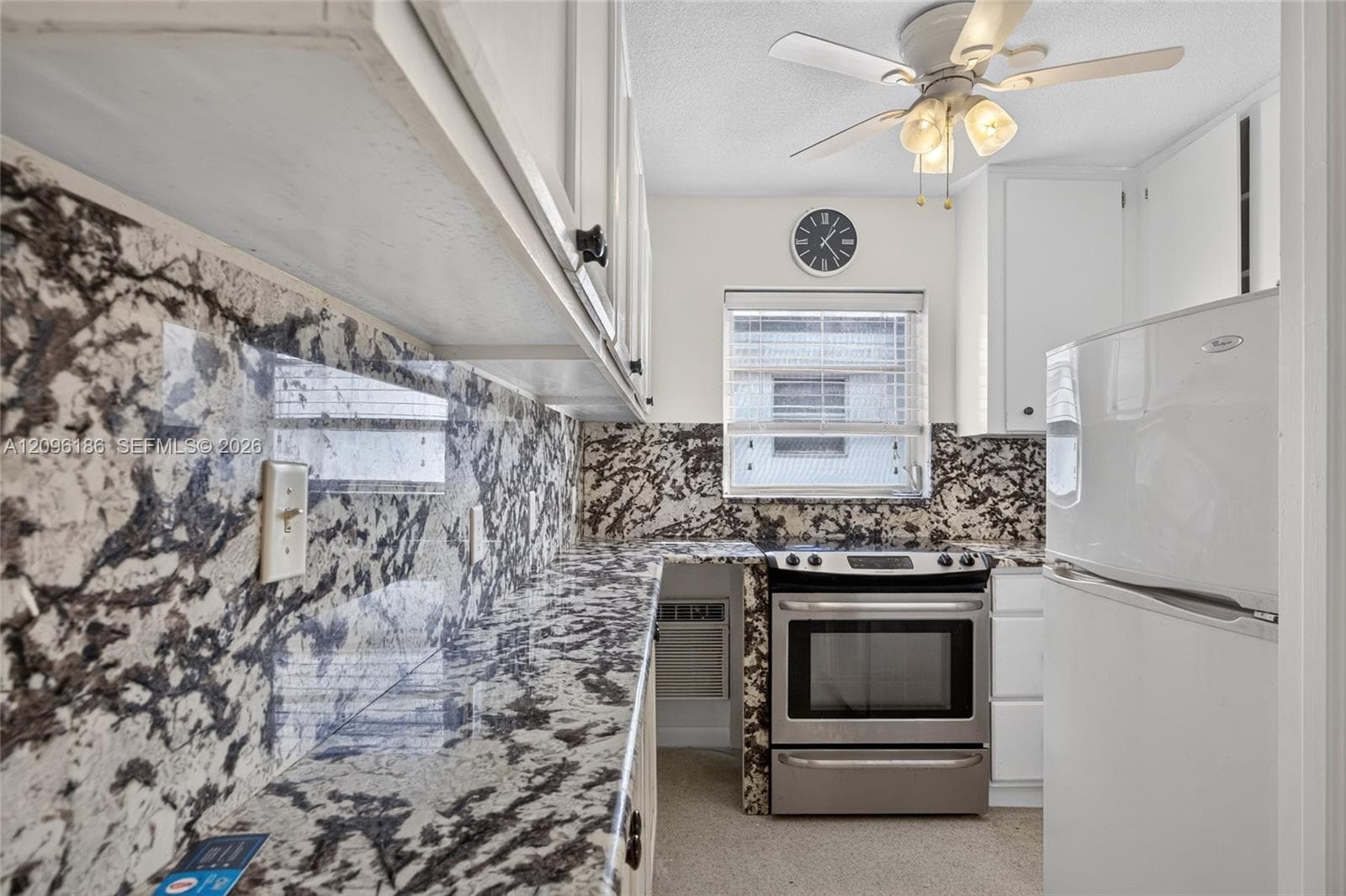 Kitchen featuring stone-patterned countertops and matching full-height backsplash, white cabinetry, stainless steel range, white refrigerator, and ceiling-mounted light fixture with fan