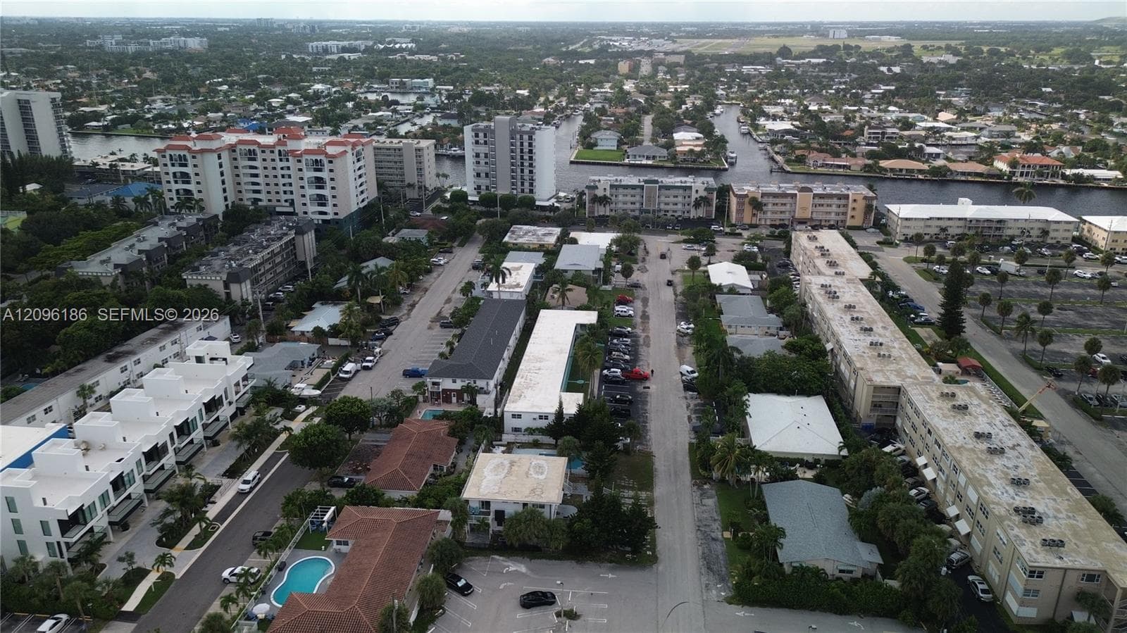 Aerial perspective of coastal residential district featuring paved thoroughfares, proximity to intersecting waterways, multi-unit developments, surface parking areas, and mature palm trees