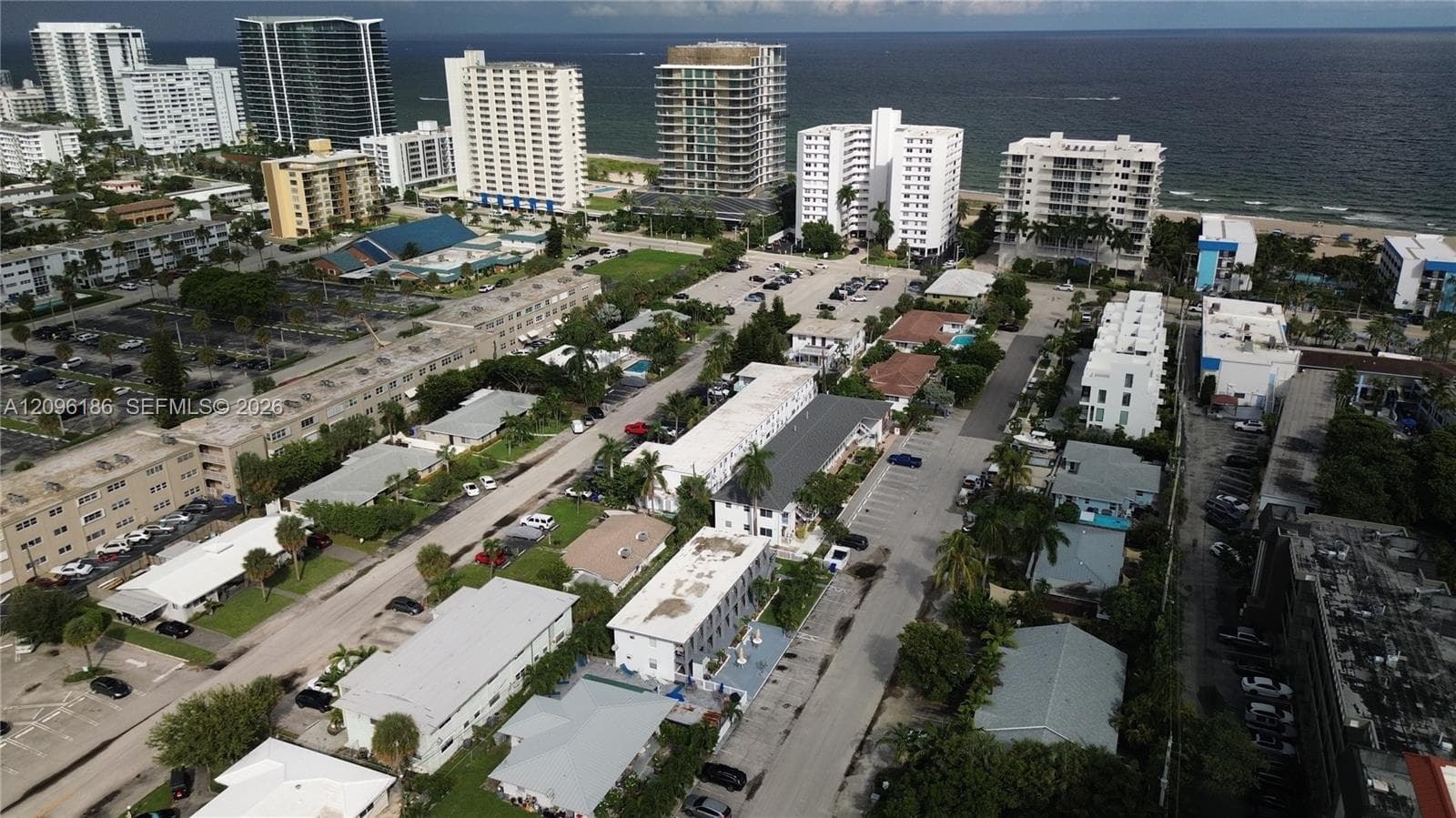 Aerial perspective featuring coastal proximity, multi-story building density, expansive paved parking lots, mature palm trees, and established street-level infrastructure