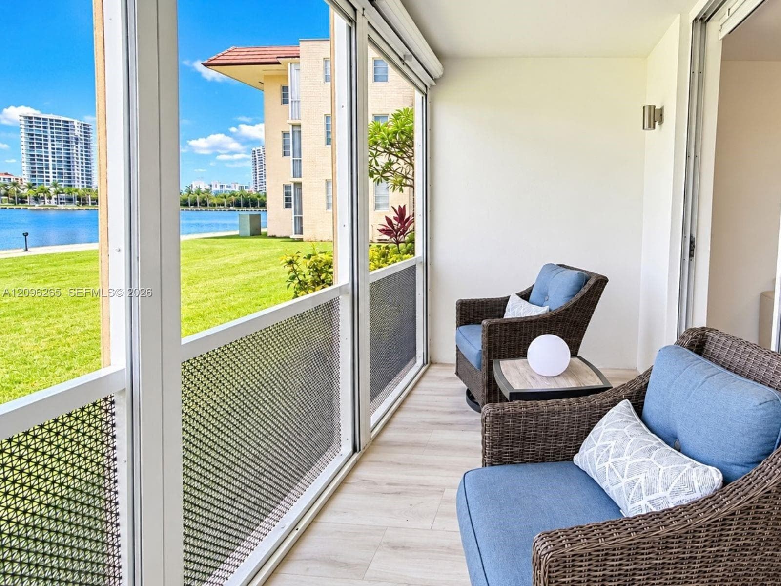 Screened balcony / sun room featuring serene bay and garden views with cozy seating area.