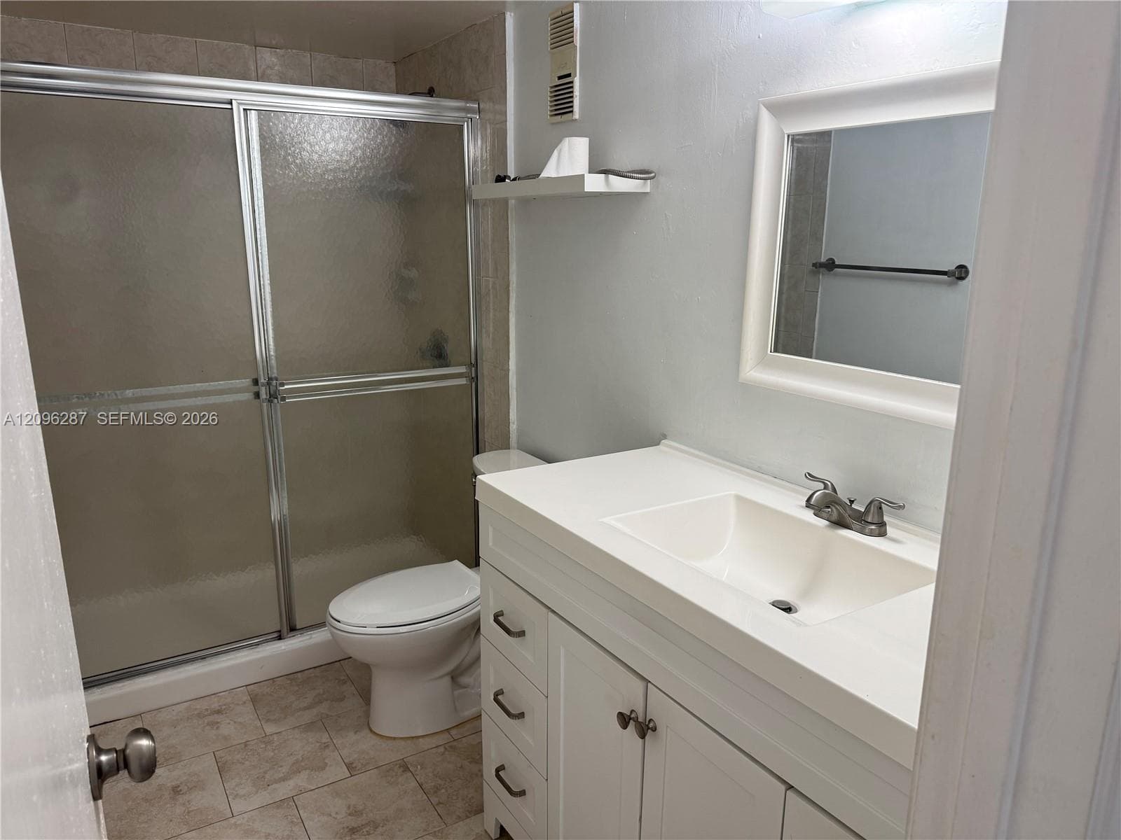 Bathroom featuring a white vanity with integrated basin, brushed metal faucet, framed mirror, walk-in shower with sliding glass doors, and tile flooring