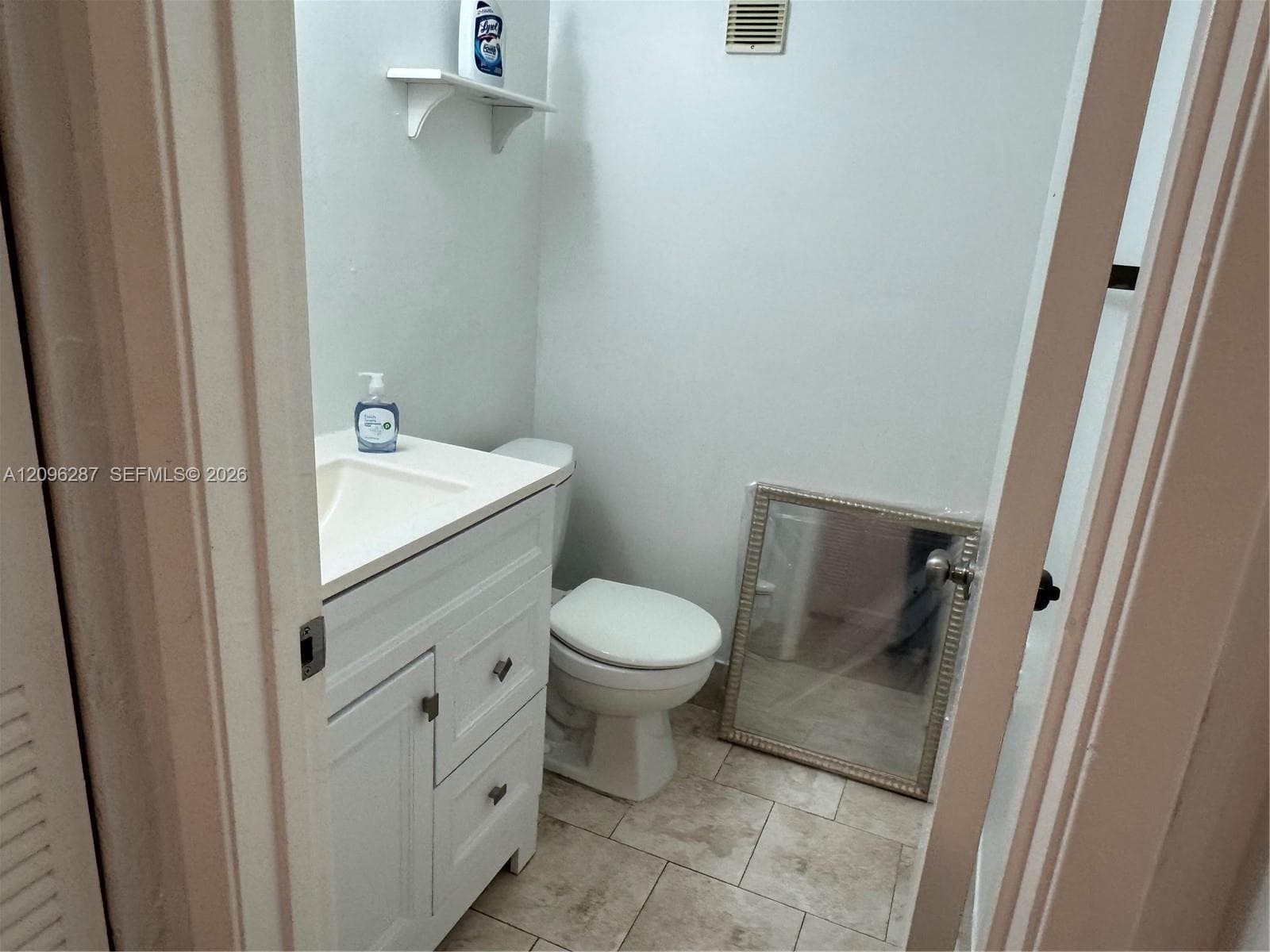 White vanity cabinet with integrated countertop, standard toilet, and stone-finish floor tile