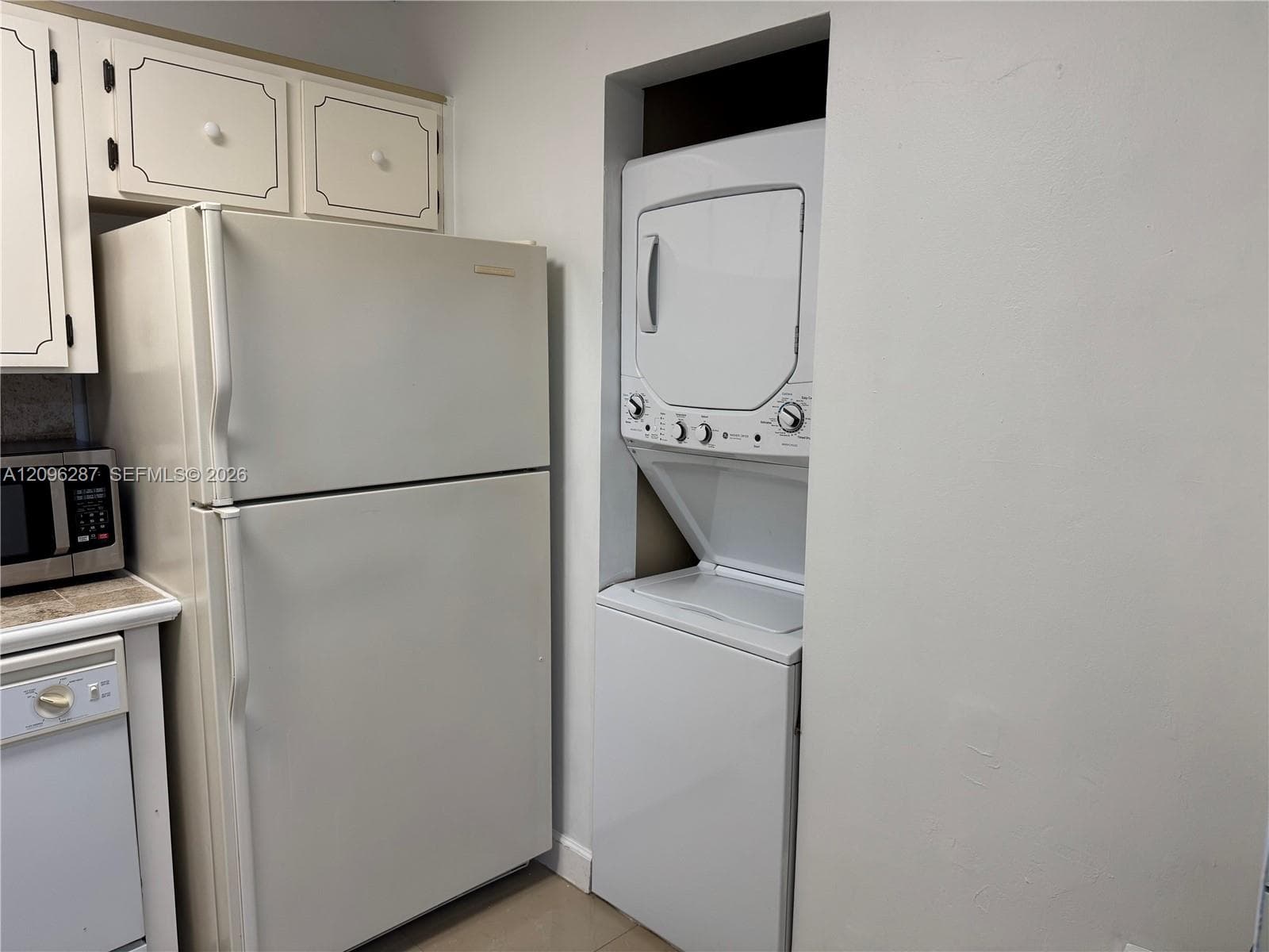 Stacked white laundry appliance set, full-size refrigerator, and shaker-style cabinetry with neutral finish