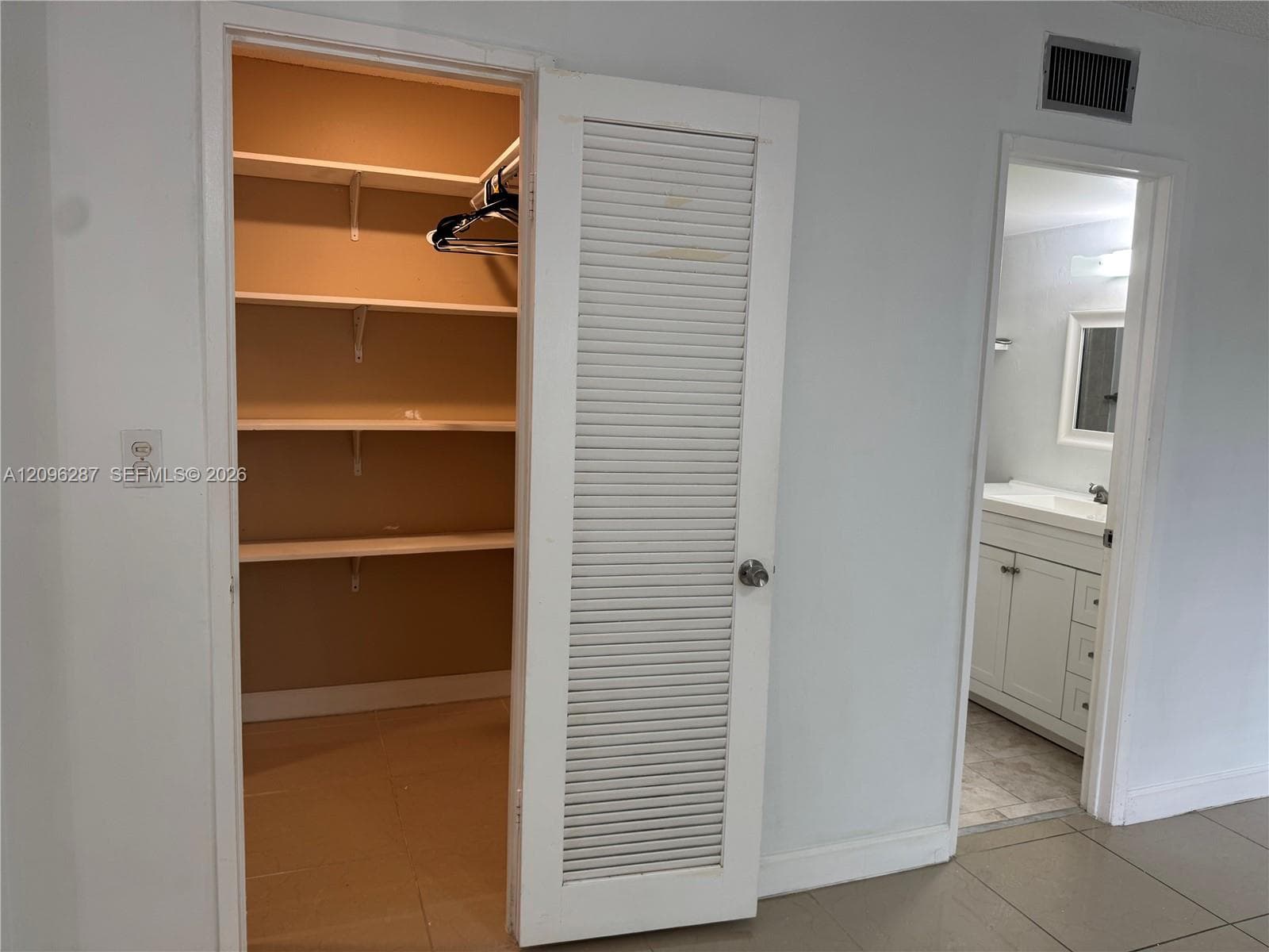Storage closet featuring built-in shelving and a white louvered door, with an interior glimpse of a vanity cabinet and solid surface countertop