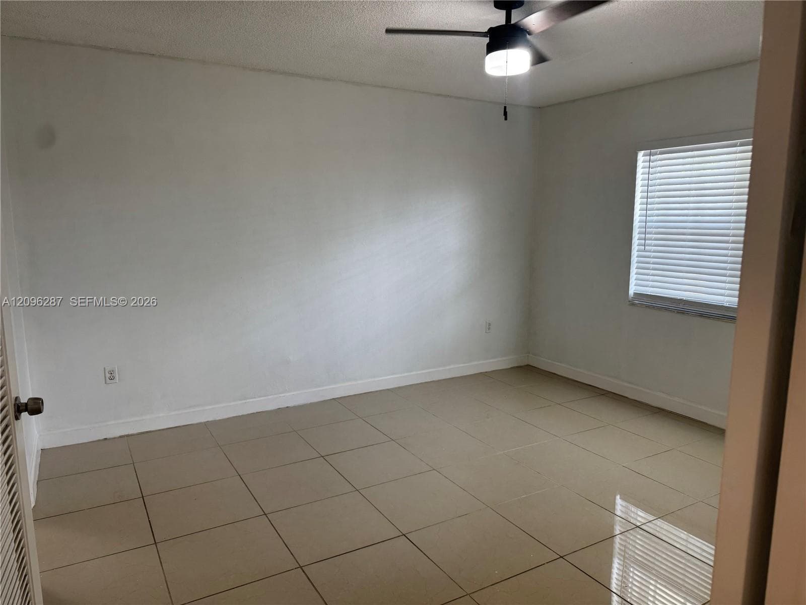 Room featuring large-format neutral tile flooring, a ceiling fan with integrated lighting, and a window with horizontal blinds