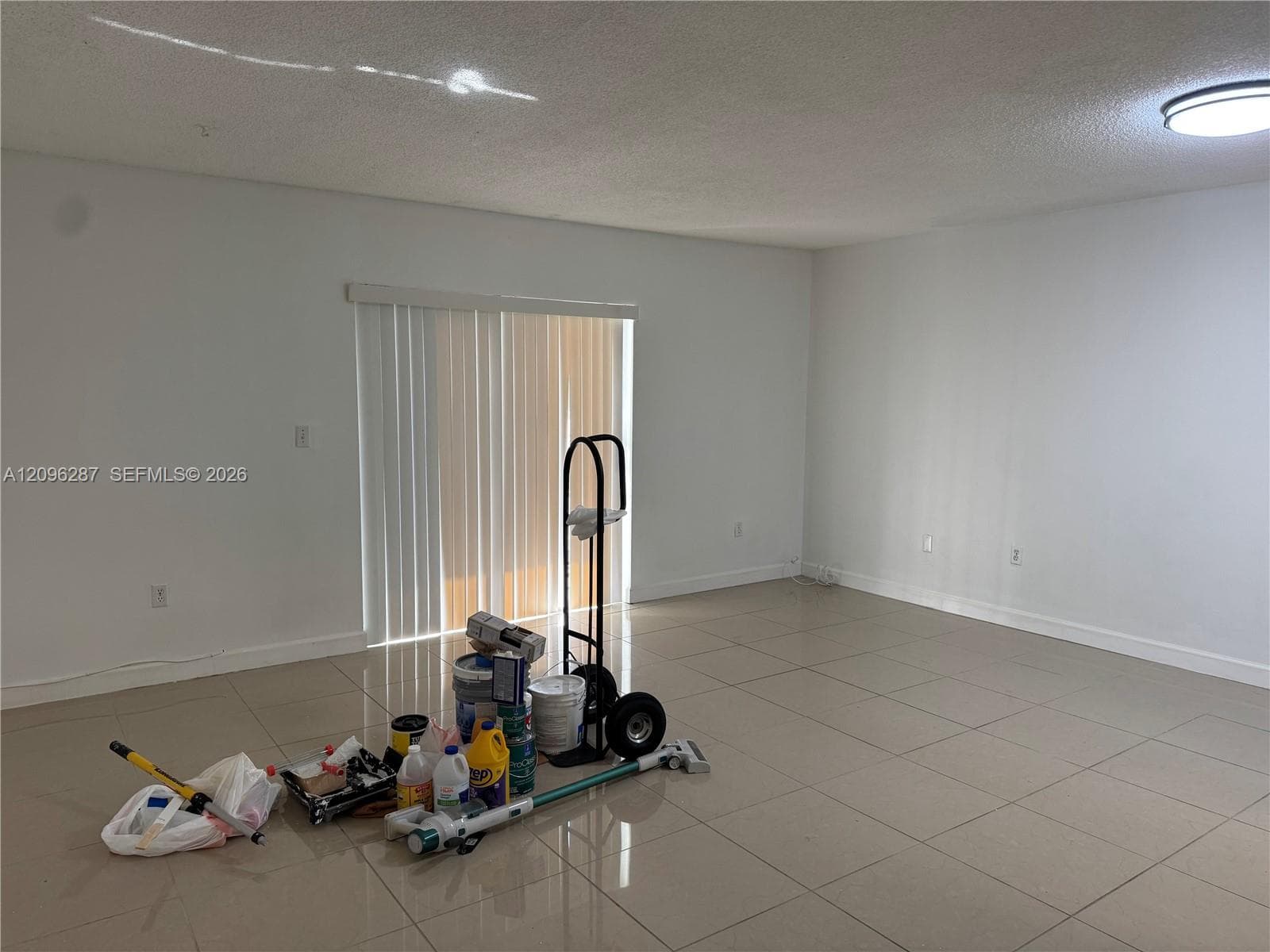 Neutral-toned tile flooring, white wall finishes, and vertical sliding door blinds