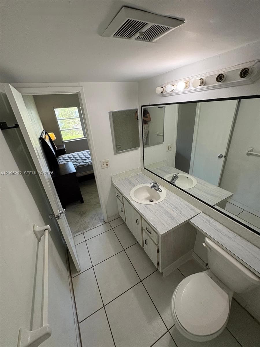 Bathroom featuring a vanity with a light-toned countertop, integrated basin, large-format tile flooring, a wall-to-wall mirror, and overhead vanity lighting