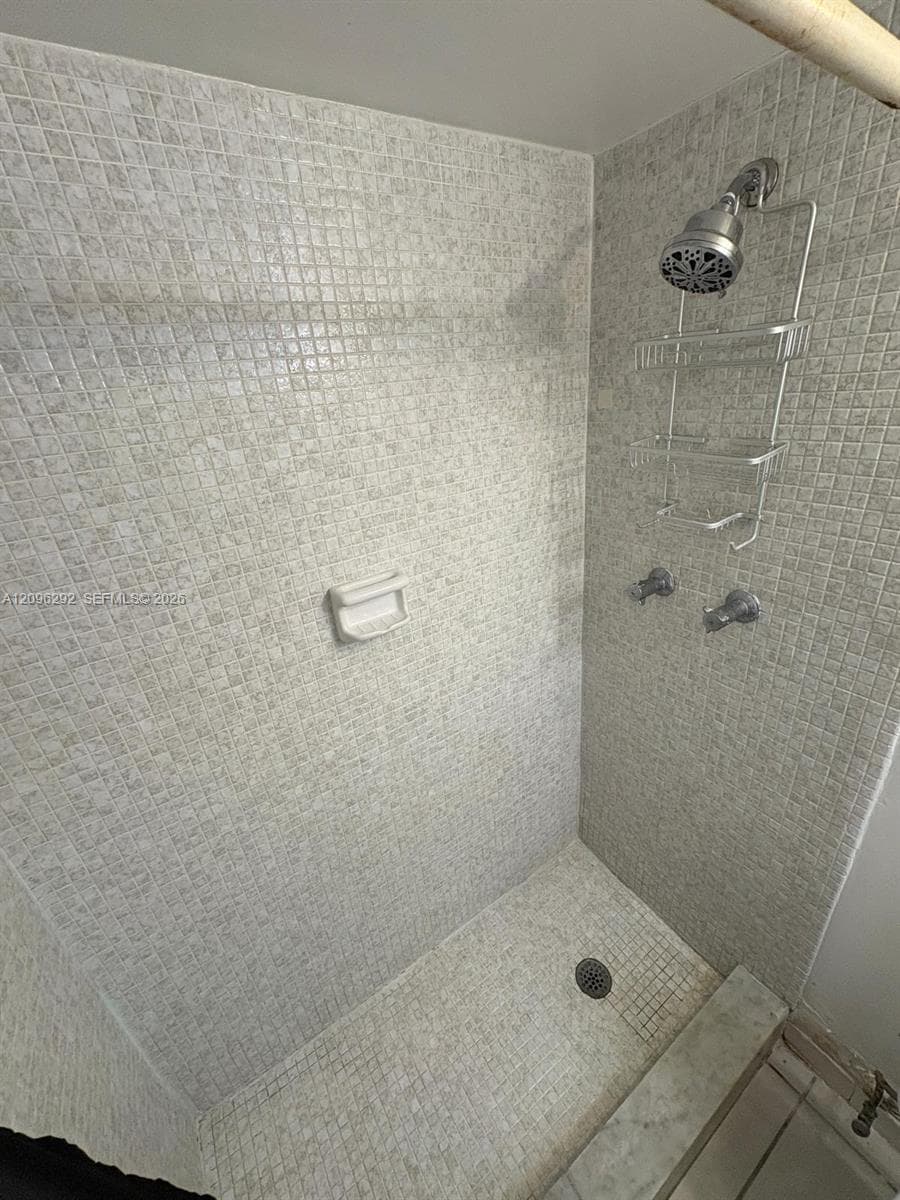 Shower enclosure featuring mosaic tile wall and floor surfaces, a built-in soap dish, and chrome-finished plumbing fixtures