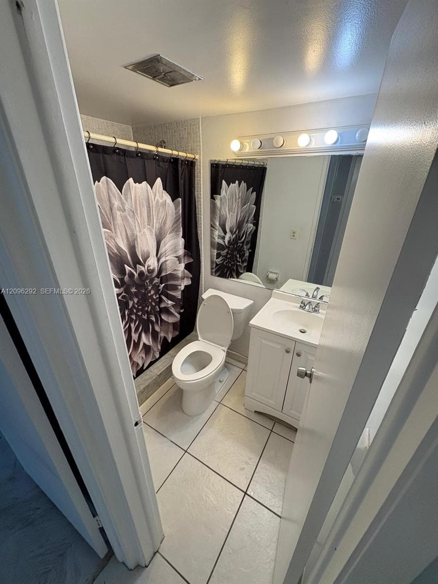 Full bathroom featuring white ceramic tile flooring, a white vanity cabinet with an integrated sink, a wide wall-mounted mirror, and a multi-bulb vanity light fixture