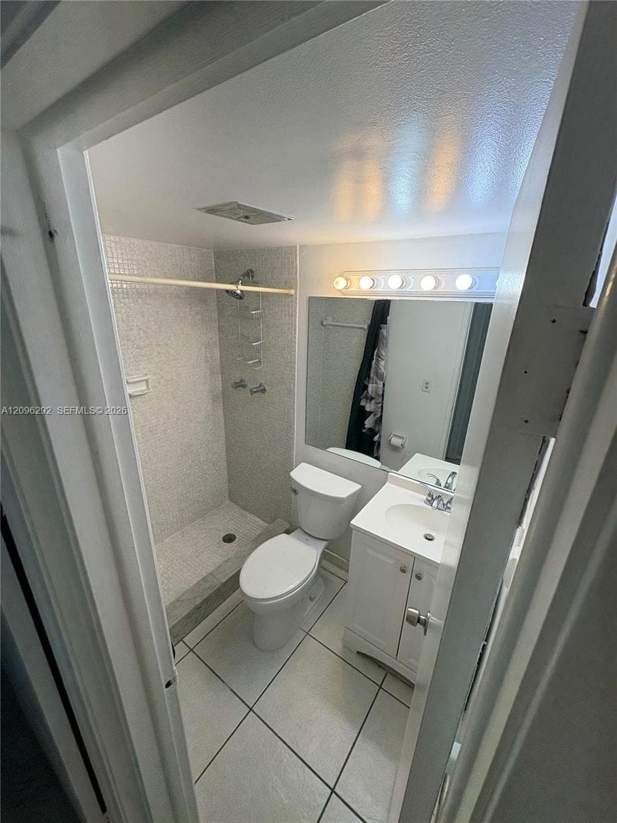 Bathroom featuring a vanity with an integrated sink, polished chrome faucet, oversized vanity mirror, multi-bulb wall lighting, and a walk-in shower with mosaic tile surround and stone-finish base