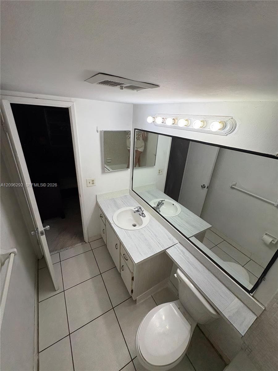 Bathroom featuring light-toned cabinetry with a solid-surface vanity countertop, integrated sink, expansive wall-mounted mirror, and tile flooring