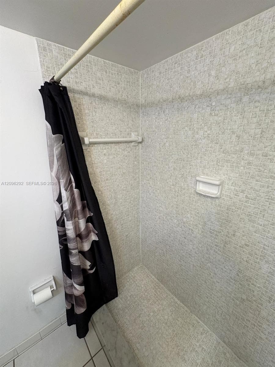 Shower stall featuring floor-to-ceiling mosaic tile wall surround, integrated built-in soap dish, and neutral-tone tile flooring