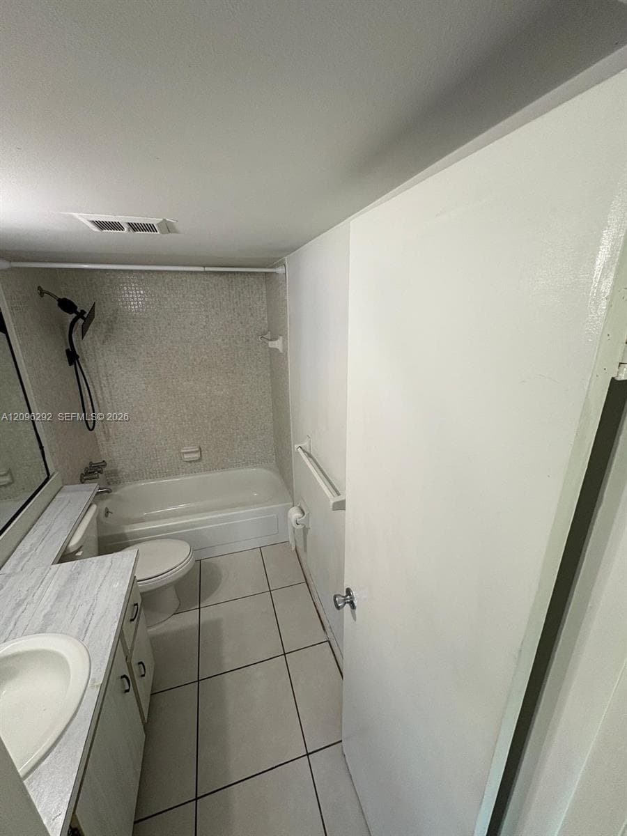 Bathroom featuring large-format floor tiling, a vanity with stone-patterned countertop, a white porcelain sink, a combination shower and tub with mosaic tile surround, and a matte black handheld shower fixture