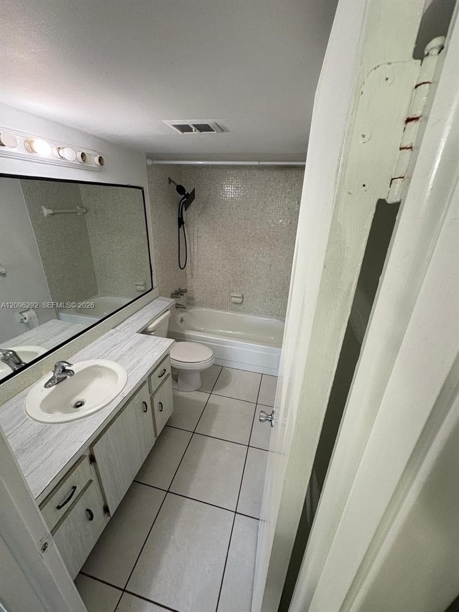 Bathroom featuring a large vanity with stone-pattern laminate countertop, integrated oval sink, full-width mirror, tile flooring, and a shower-tub combination with tiled surround