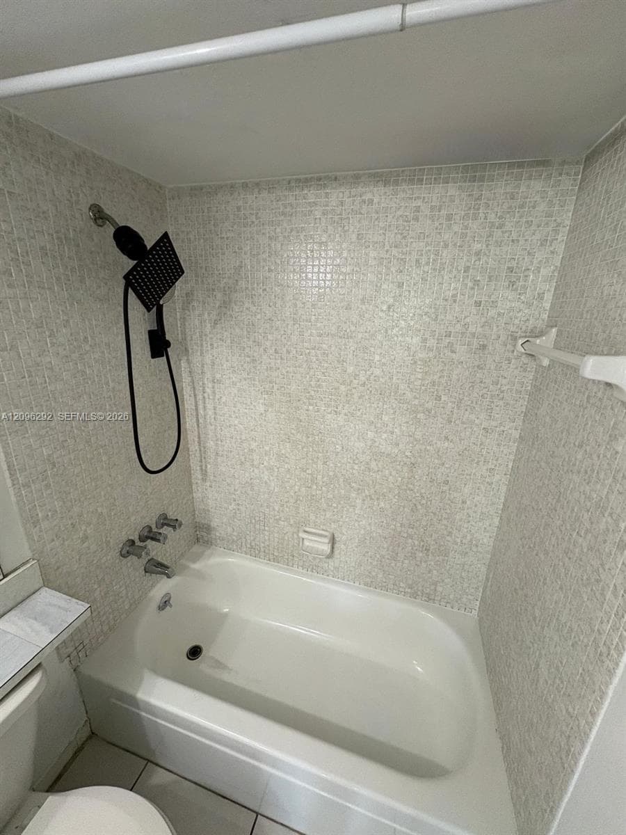 Bathtub with white porcelain finish, mosaic tile surround, and black rainfall showerhead