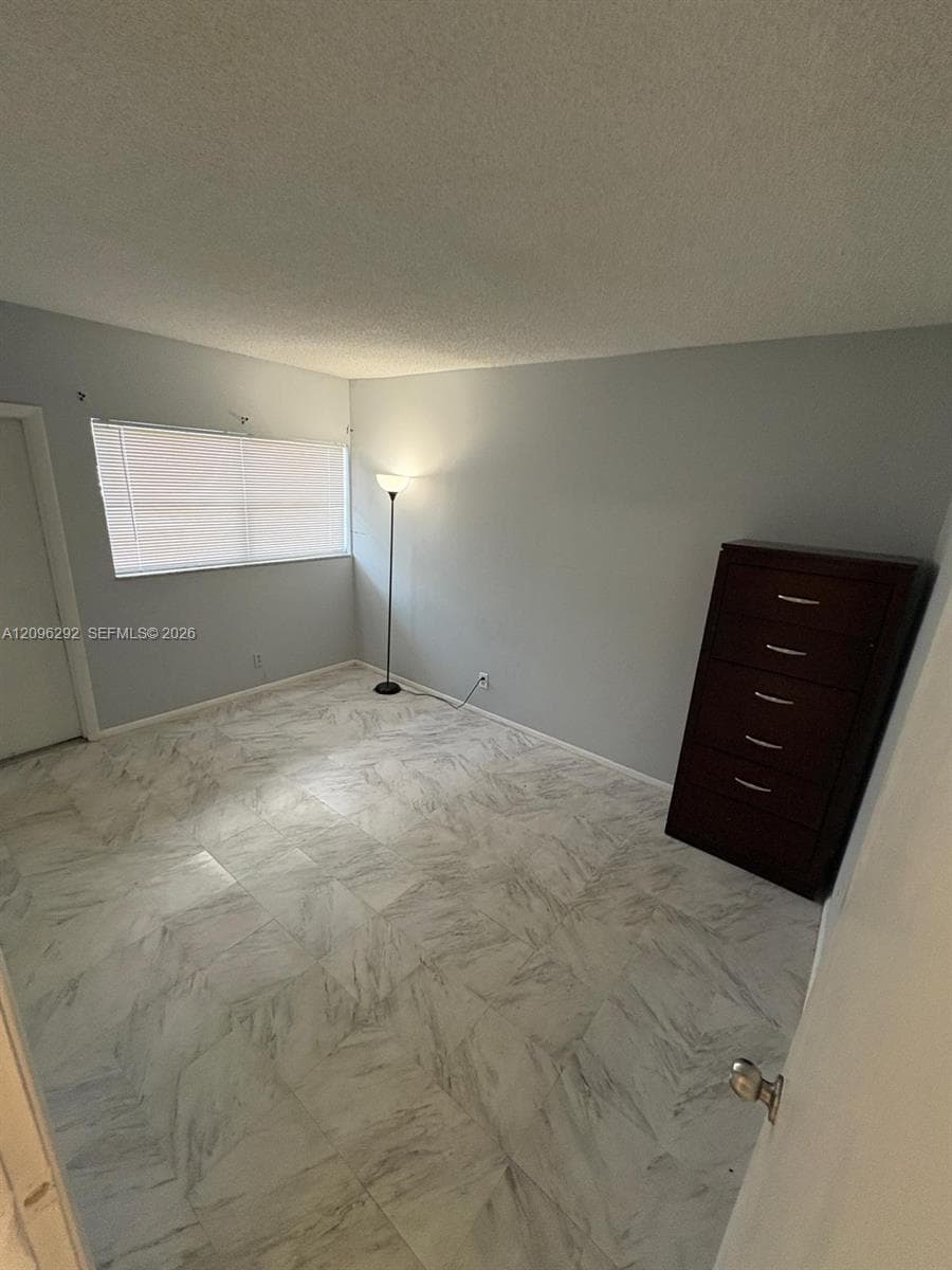 Room featuring patterned stone-finish tile flooring, neutral wall paint, and a rectangular window with horizontal blinds