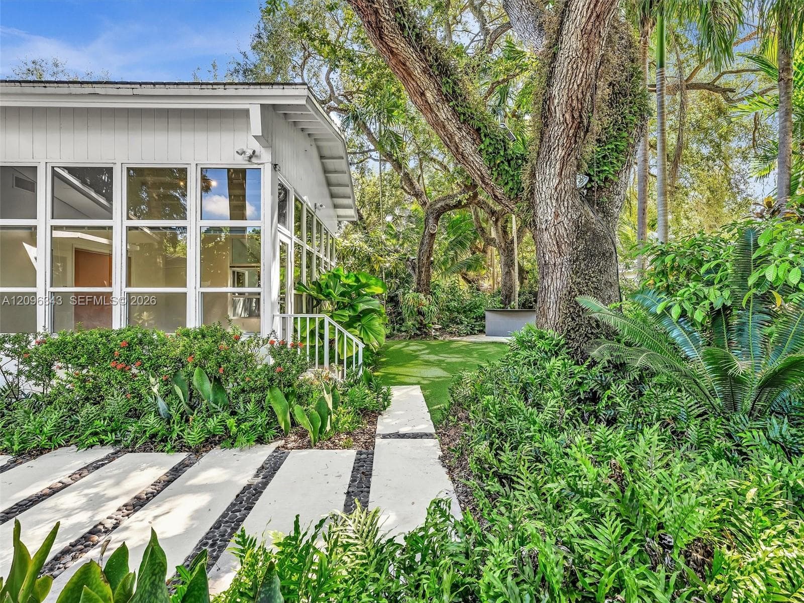 Bright sun room spills to landscaped yard with turf and concrete landing paths.  House for rent in Coconut Grove.