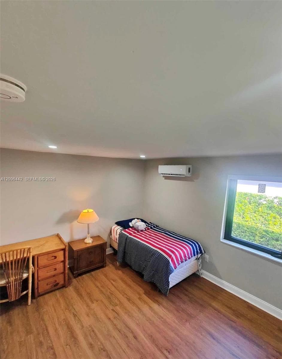 Interior space featuring wood-finish flooring, recessed lighting, a wall-mounted ductless climate control unit, and a window with exterior scenery
