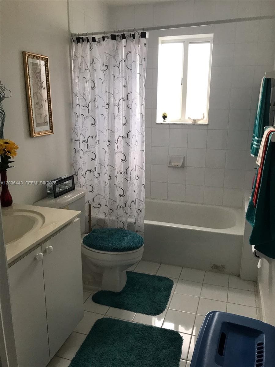 Bathroom featuring white tiled walls, a bathtub with an integrated shower, a white vanity with an inset sink, and a window providing natural light